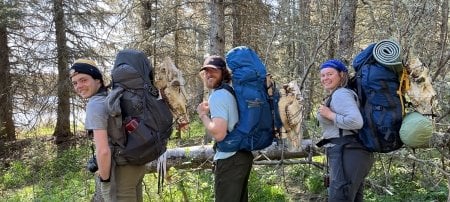 Three students hold loaded backpacks and moose skulls on their backs as they conduct field research at Isle Royale National Park for Michigan Tech.