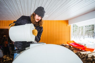 A student pours a bucket of maple sap into a large white storage drum.