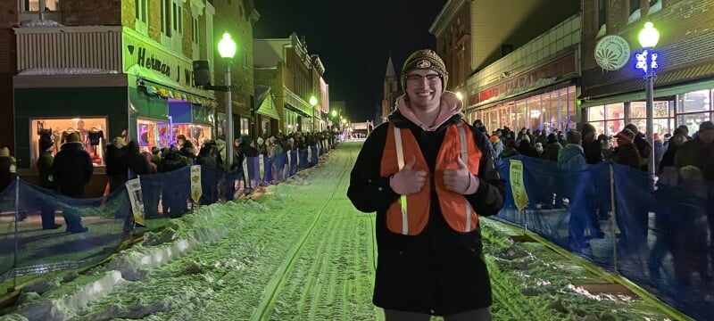 Daron Hebeler standing in the street at the Copper Dog sled races with spectators lining the sides.