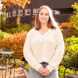 Elise Buzzell standing on campus covered in fall leaves.