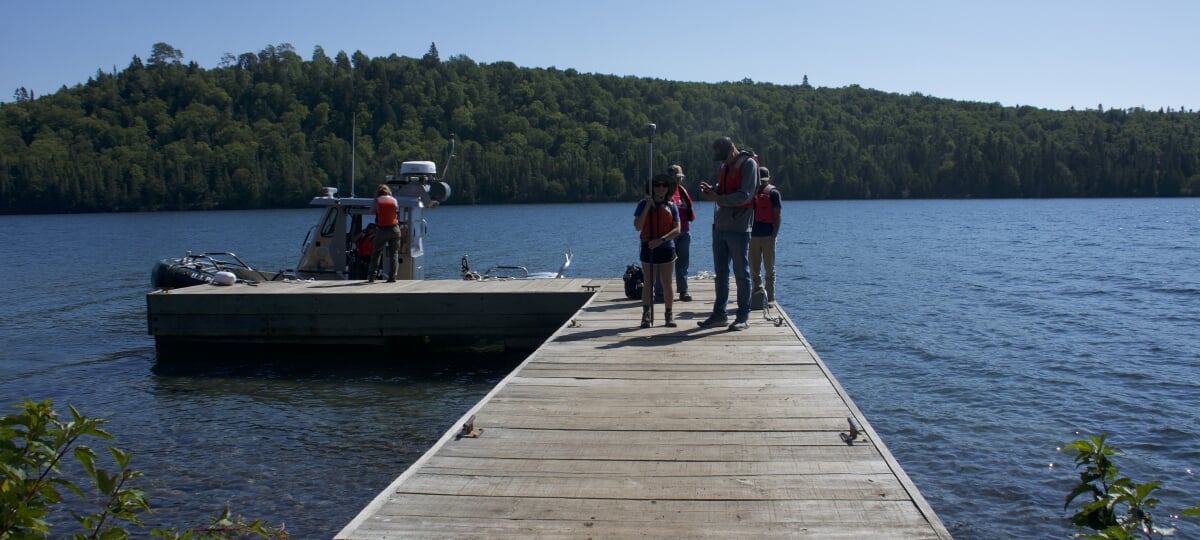Students in protective gear standing on a dock with a small boat.