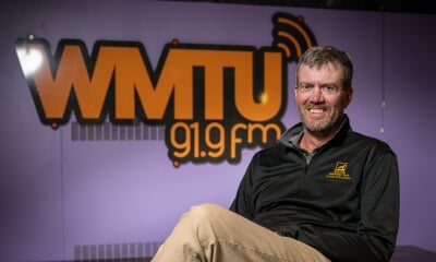 Roger Woods in the WMTU studio with a large WMTU 91.9fm sign on the wall behind.