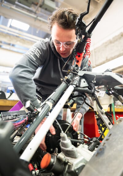 Jared Ott wears a grey sweatshirt and works with his hands on an internal mechanism of a snowmobile.