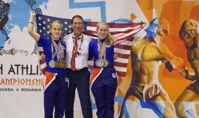 Haley Peterson, right, poses with her coach David Sixel and sister Nicole holding an American flag on the first-place podium at the 2024 Pangration Athlima World Championships in Timisoara, Romania.
