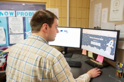 Ethan Rice sitting at a desk with the Winter Carnival 2026 website on the computer screen.