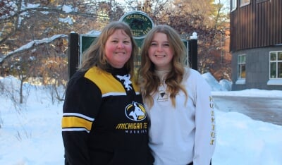 Kallee McCone and her mother, Erica Roose, both wearing Michigan Tech sweatshirts, stand together in front of a historic site marker near Rekhi Hall on Michigan Tech's campus.