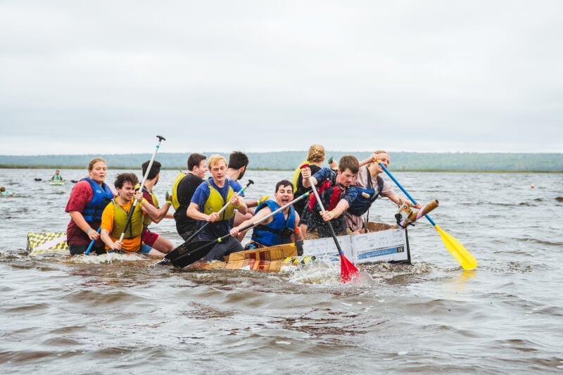 Ten Michigan Tech students wearing life jackets paddle a cardboard boat to shore during a homecoming weekend race on the Keweenaw Waterway near Chassell, Michigan.