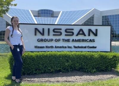 Ashley Baird standing on the grass in frong of a sign reading Nissan Group of the Americas Nissan North America Inc. Technical Center.