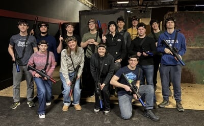 A group of students wearing headbands and holding laser tag equipment pose together inside during a Thompson Scholars Association social event.