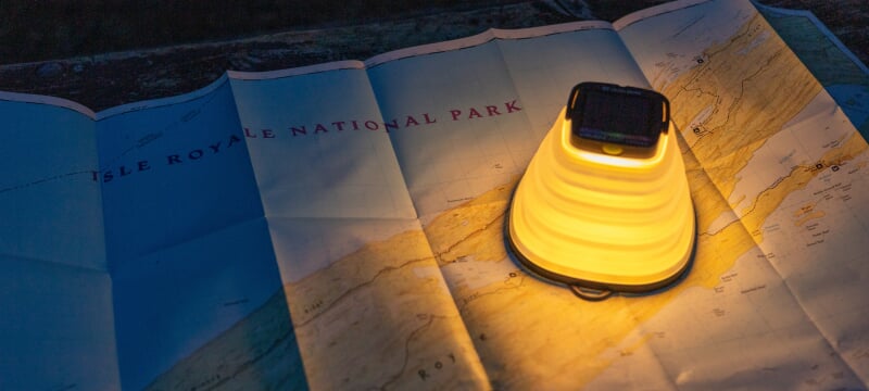 A small artificial lamp sheds dramatic yellow light on a paper map of Isle Royale National Park unfurled on a table.