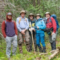 Jacob Sutter stands in the forest, posing and smiling for the camera with four volunteers wearing hiking gear.