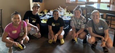 Students from the Thompson Scholars Association pose indoors with bins of supplies during a 31 Backpacks volunteer event.