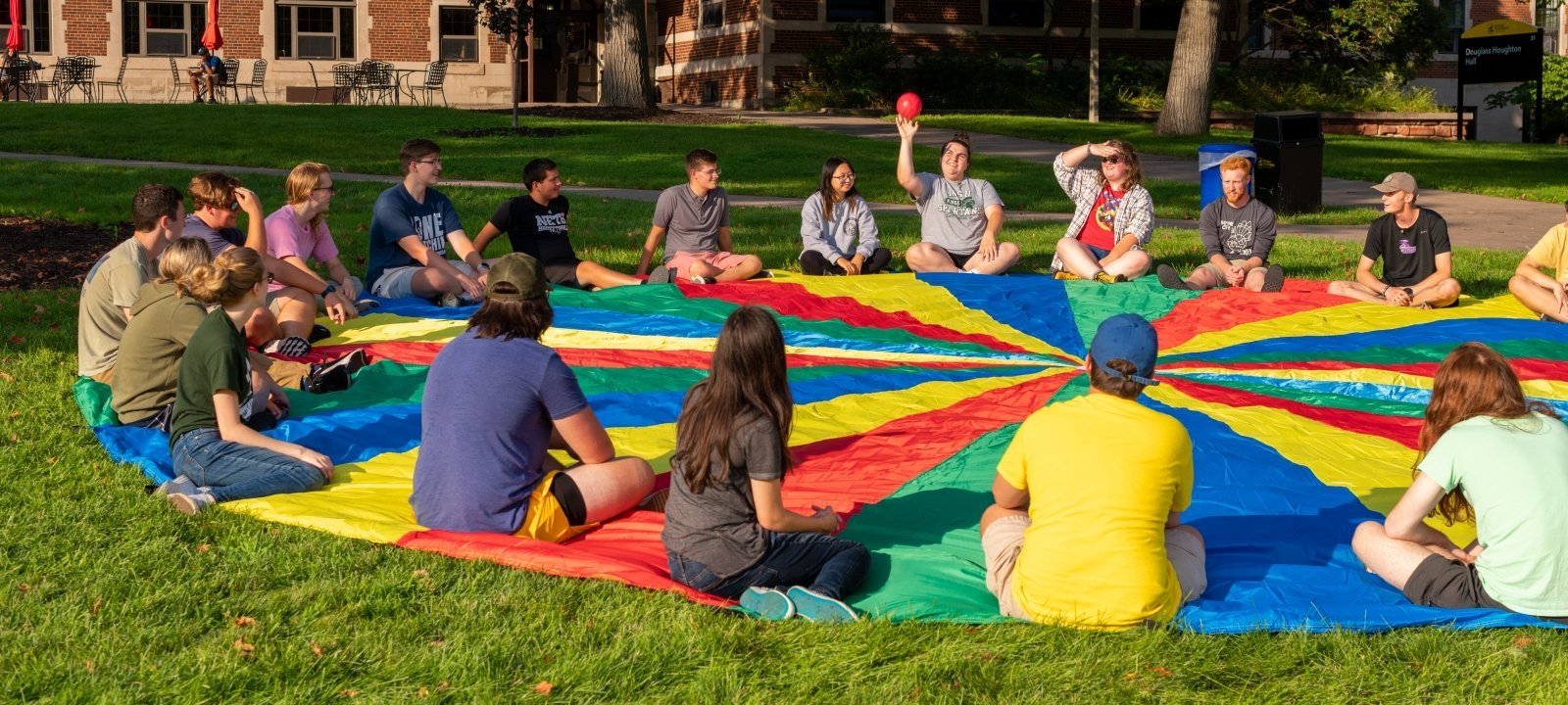 Students sitting on a multicolored parachute playing a game