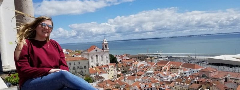 A student sitting on a balcony in Italy overlooking a small town and the sea.