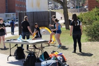 Students playing with a soccer ball near a table on campus.