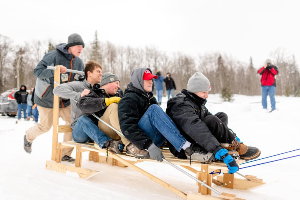 Four men on a wood sled being pushed by another man