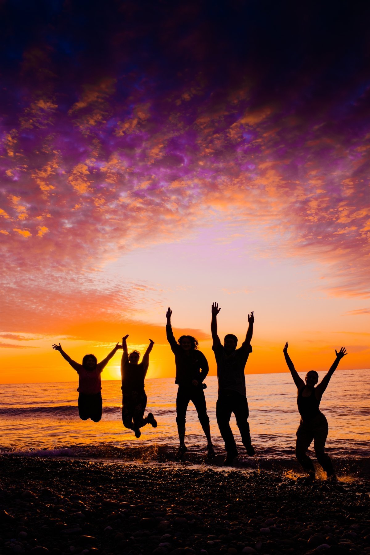 Silhouette of students jump on a beach at sunset.