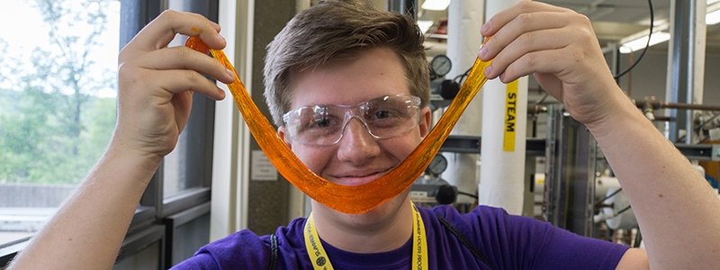 A young man smiles while holding a smile of slime in front of his face.