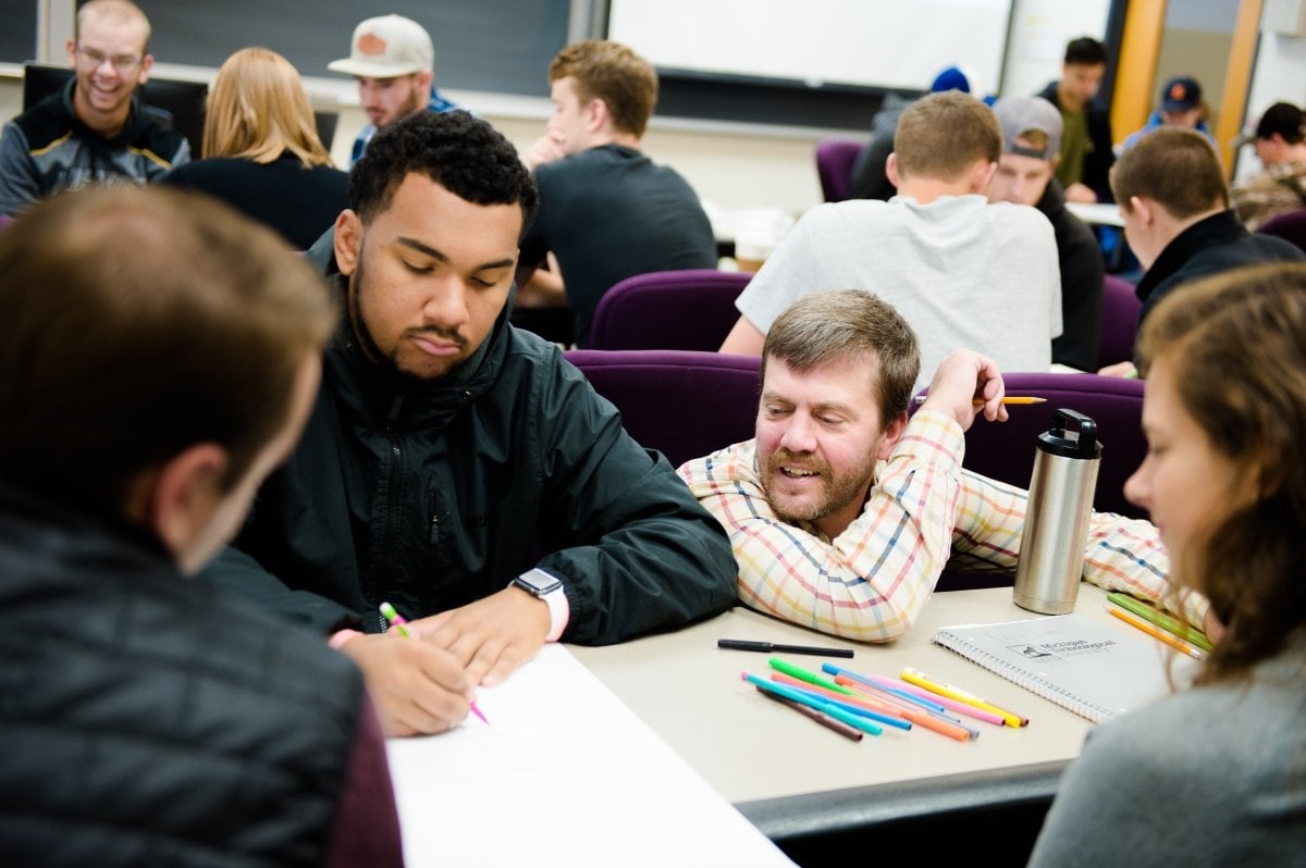 Faculty helping students at a classroom table.