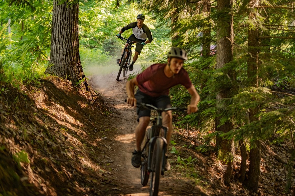 Two people riding mountain bikes on a forested trail.