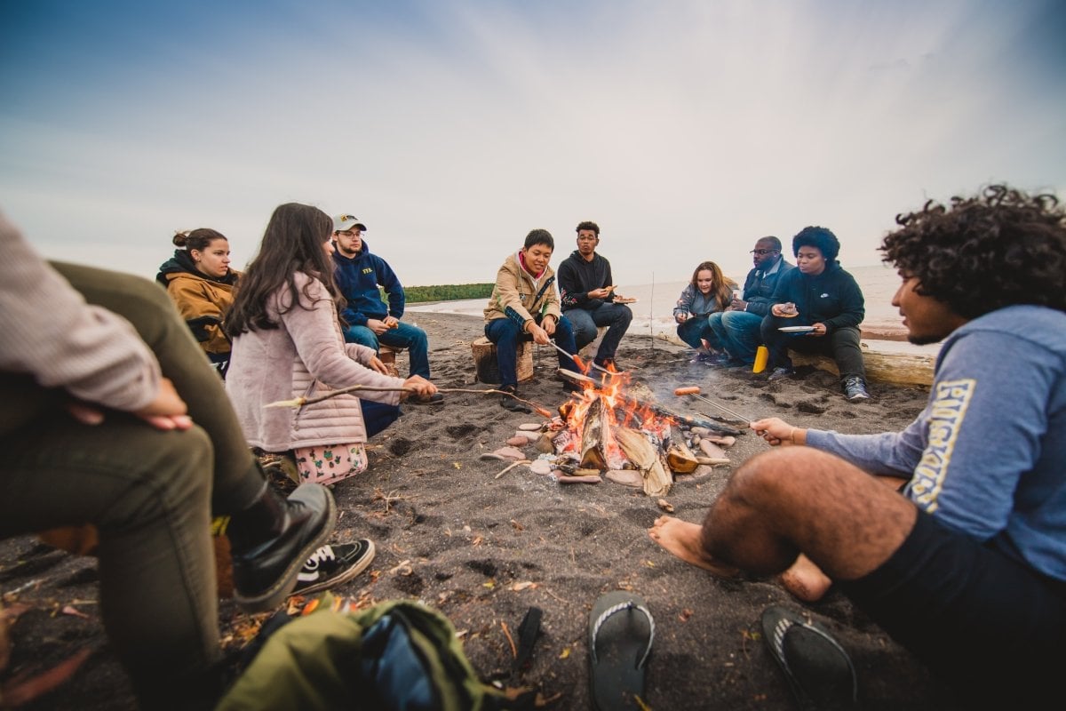 Students sitting on a log enjoying a camp fire.