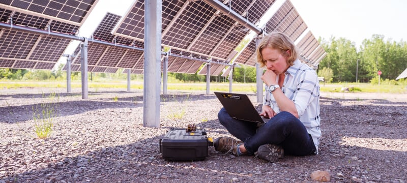 Research sitting next to solar panels looking at a laptop.