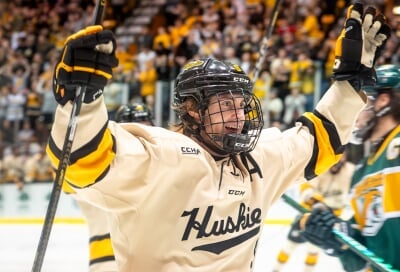 Huskies Hockey player in a white jersey celebrating with his arms raised.
