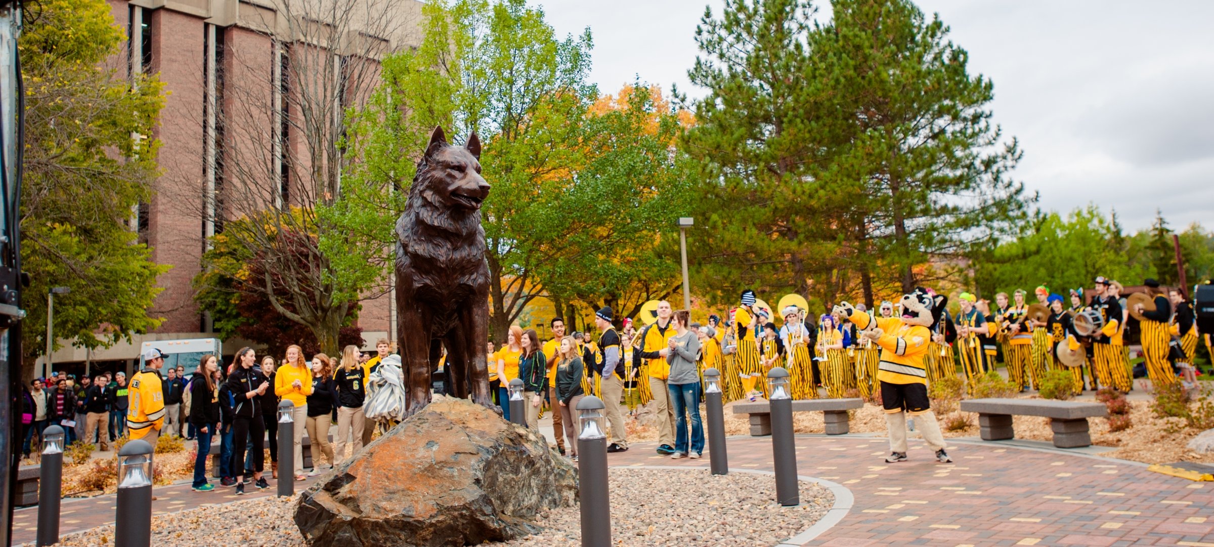 The pep band, Blizzard T. Husky, and other people gathered around the Husky Statue.