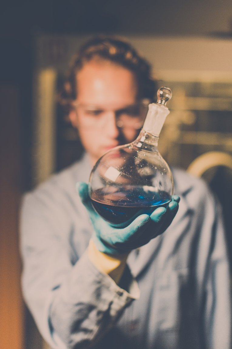 Luck Lab Vertical Undergraduate Randy Wilharm holds up a flask containing a ligand complex that may help create a biomass fuel.