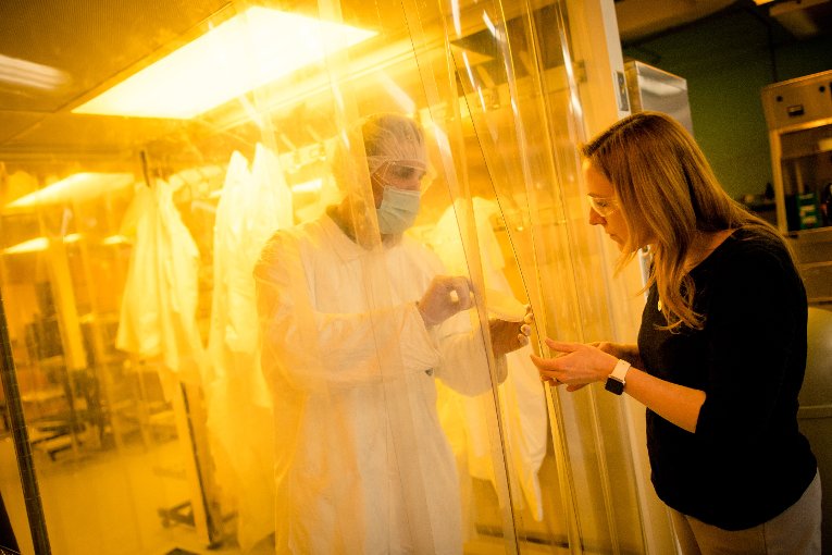 Researcher showing a sample to another person from behind the clean lab barrier.