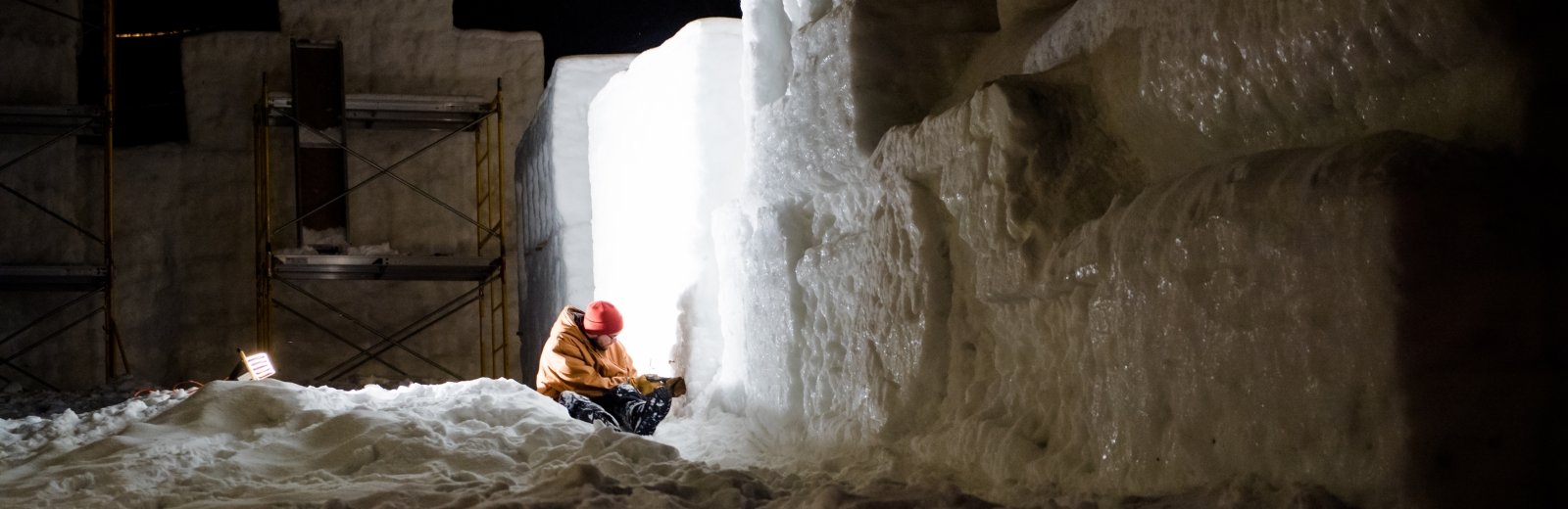 A student chisels the side of a snow statue at night.