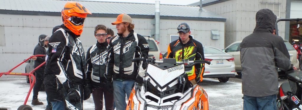 A group of engineering students stand around an orange snowmobile. 