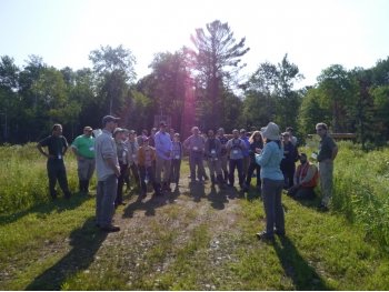 a group of people stand in semicircle in an open meadow