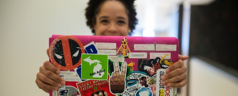 young woman holding out a pink laptop with stickers on it