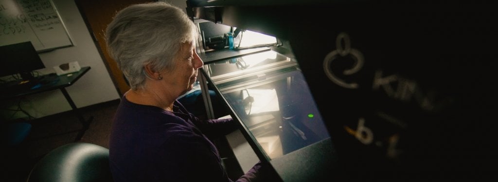 older woman sits at a table in front a robot with handles