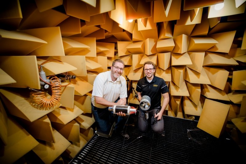 two men kneel on a grate in a room covered in yellow foam wedges