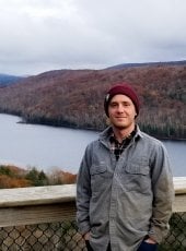 young man in hat standing in front of a river