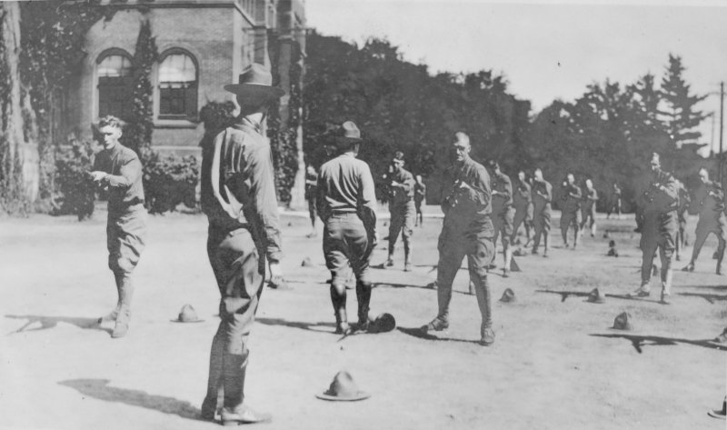 a 1918 photo of men practicing combat drills with wooden bayonets outside on a campus