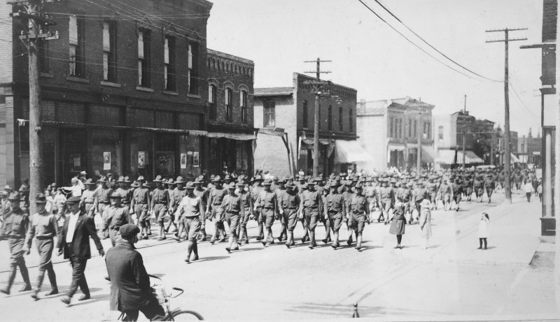 troops marching in uniform in formation down a downtown city street in Houghton Michigan in 1918