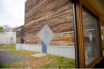 A diamond-shaped clear decal with traced lines on a window overlooking a wooden building outside with a door and with green glass.