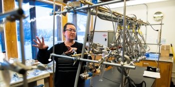 A women speaks while standing behind a vacuum line suspended from a ceiling in the Carbon, Water and Soils Lab.