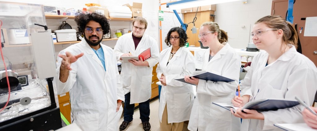 group of people standing in lab wearing coats and protective glasses