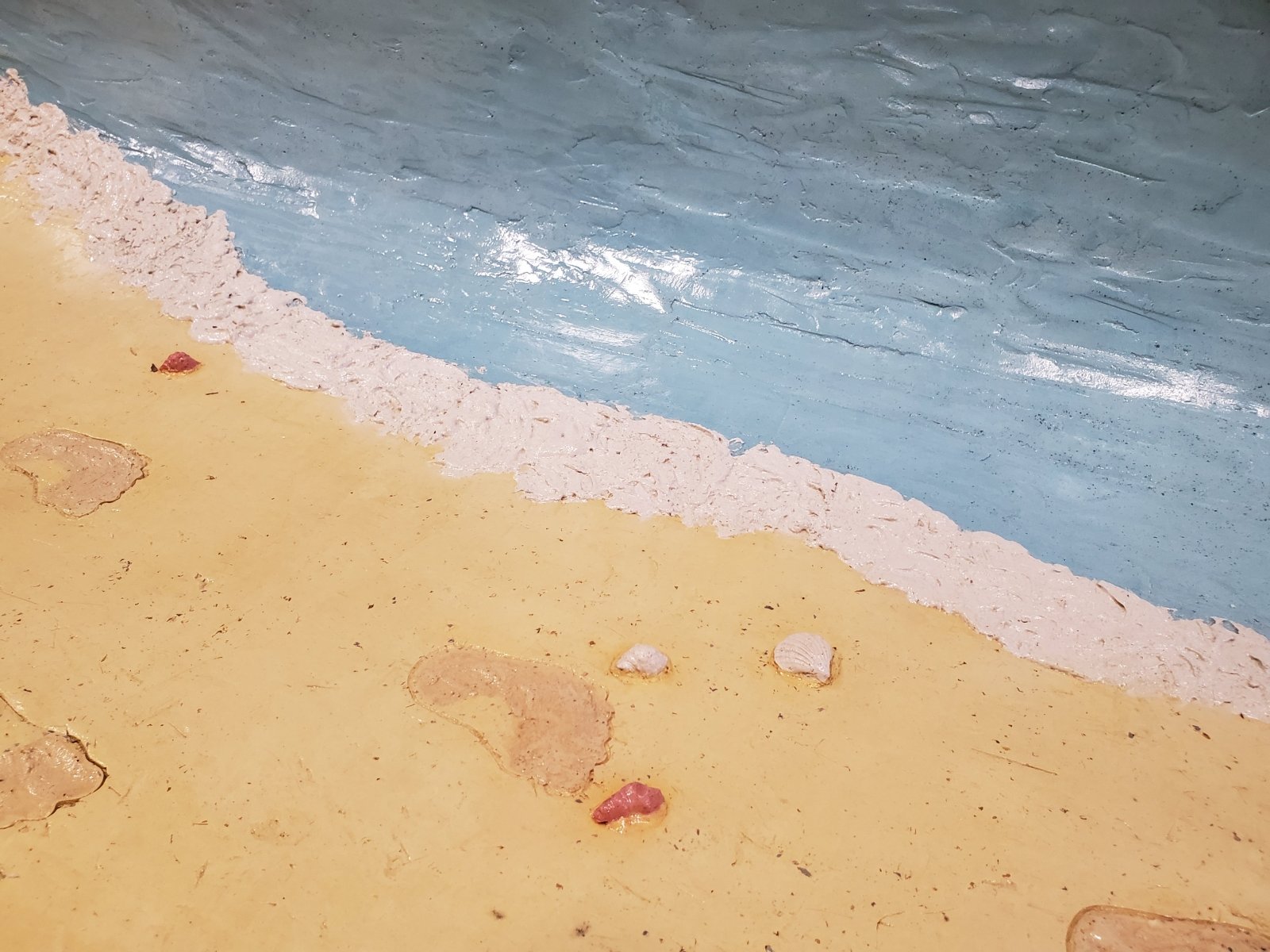 plaster molded to look like blue water with a wave at the shore, a tan shore, with sandy footprints and seashells. (Photo credit: Charlie Hill) 