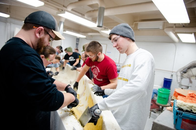 students with safety glasses and gloves mold a boat made of concrete