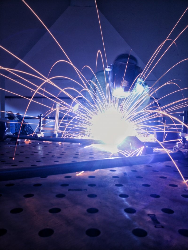 A student in welding gear welds and arcs sparks in a shop