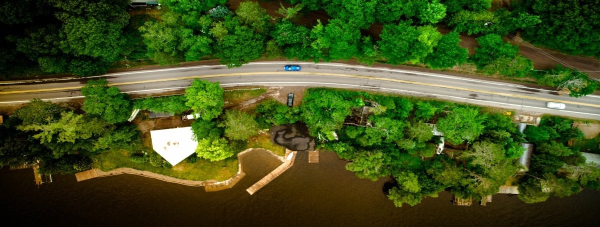 drone image overhead of road with blue car and trees