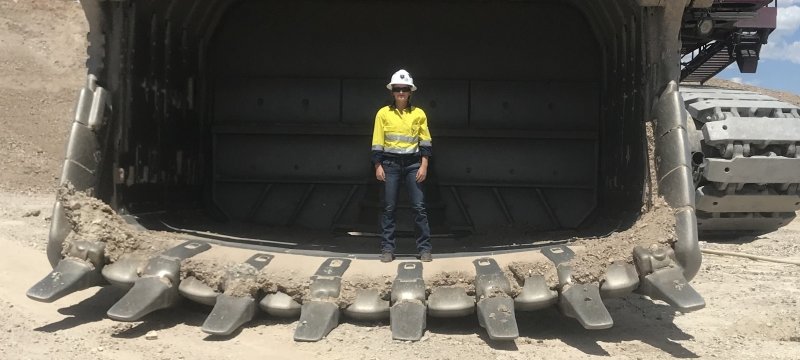 woman in a hard hat standing next to a 20-foot tall mining truck