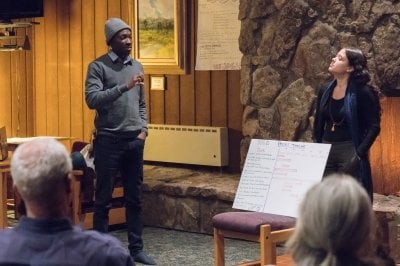 A man and a woman stand before an audience talking about a poster.