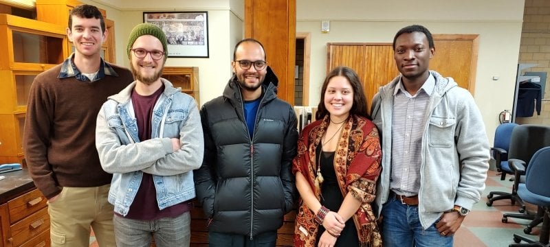 Five people—four men and one woman—stand in a row, smiling.