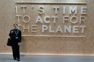 Alexis Pascaris stands in front of lettering on a wall that reads "It's time to act for the planet."